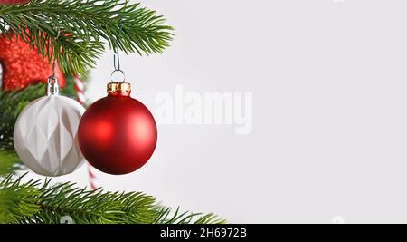 Banner a forma di sfera rosso Natale baubles su albero di Natale sul lato di grigio sfondo bianco con spazio copia Foto Stock