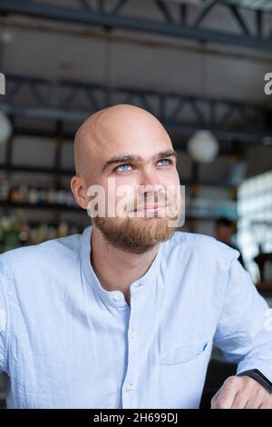 Ritratto di calvo bianco europeo con barba e occhi grigi in camicia blu chiaro nello spazio di lavoro Foto Stock