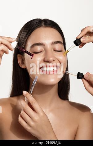 Cura della pelle. Bellezza Ritratto della donna, mani che cadono siero collagene idratante sul viso. Modello che utilizza il prodotto cosmetico naturale per idratato, incandescente e. Foto Stock