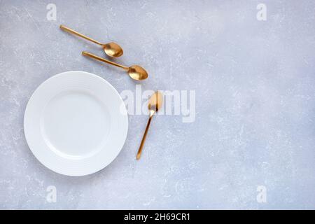 tre cucchiai da dessert dorati vicino a un piatto vuoto sullo sfondo grigio, concetto di tre persone partecipanti, vista dall'alto, spazio per la copia Foto Stock