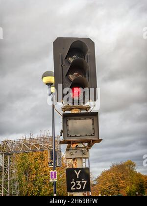 Luce di segnalazione per i treni alla fine di una piattaforma impostata su rosso. Un segnale di testa e gli alberi sono sullo sfondo e un cielo nuvoloso è sopra. Foto Stock