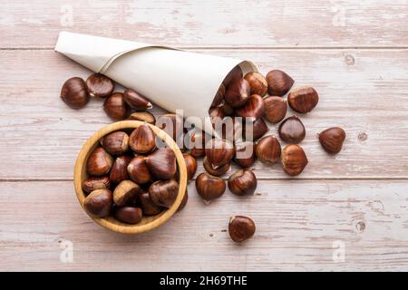 Cornet di castagno e ciotola di legno con castagne su un tavolo di legno chiaro Foto Stock