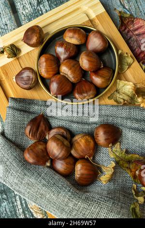 Deliziose castagne su piatto d'annata e panno grigio. Autunno ancora vita con foglie cadute Foto Stock