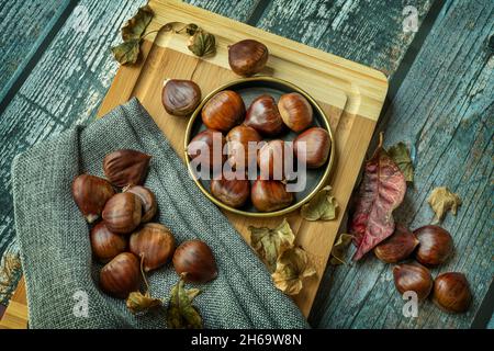 Deliziose castagne su piatto d'annata e panno grigio. Autunno ancora vita con foglie cadute Foto Stock