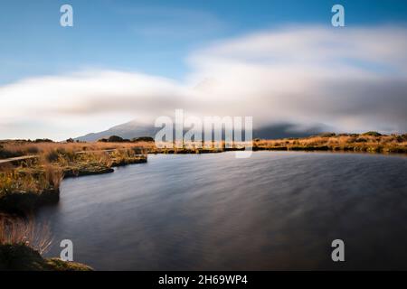 Il monte Taranaki è quasi invisibile, coperto da nubi in rapido movimento. Tempo variabile a Pouakai tarn nel Parco Nazionale di Egmont. Foto Stock