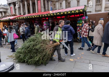 Un lavoratore porta un albero di Natale al mercato di Natale, Trafalgar Square, all'inizio della stagione festiva 2021 Natale nella capitale, Londra, Inghilterra. Foto Stock