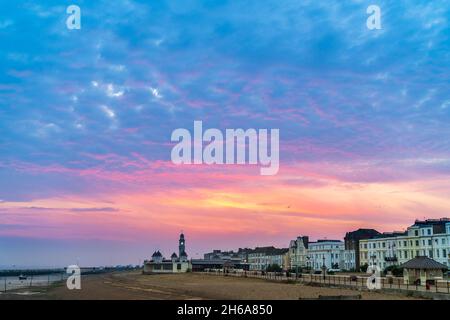 Il cielo dell'alba sul lungomare della cittadina turistica inglese di Herne Bay. Cielo colorato sopra la spiaggia e gli edifici sul lungomare con una torre dell'orologio. Foto Stock