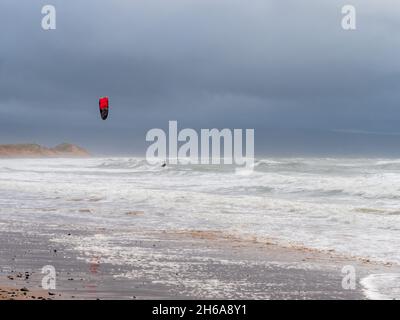 Un kitesurfer surf lungo le onde sulla spiaggia contro un cielo tempestoso e nuvoloso Foto Stock