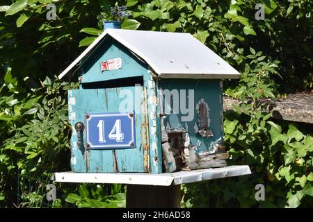 Una mailbox fatta in casa, una scatola in legno color turchese a forma di casa con tetto a falde e l'intera apertura frontale su cerniera a piano Foto Stock
