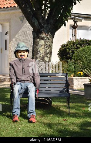 Un uomo di paglia, una figura umanoide piuttosto cremosa, piena di dimensioni, che si rilassa su una panca, in un giardino suburbano al limitare della città Foto Stock