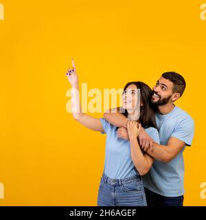 Buona offerta. Ritratto della coppia araba abbracciando, guardando e puntando lo spazio di copia su sfondo giallo, uomo e donna dimostrando il posto libero per il vostro Foto Stock
