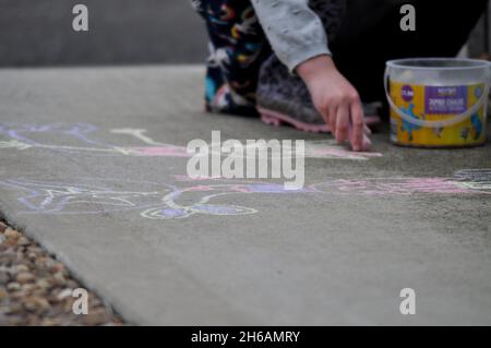 Bambino che utilizza gessi jumbo per disegnare all'esterno su cemento Foto Stock
