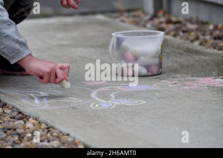Bambino che utilizza gessi jumbo per disegnare all'esterno su cemento Foto Stock