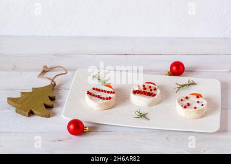 antipasto di fine anno a base di formaggio rotondo e bacche di pepe, sfondo bianco in legno, vista laterale Foto Stock