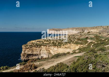 Costa calcarea rocciosa dell'isola di Gozo e del Mar Mediterraneo con acque turchesi blu e grotte. Verdi campi terrazzati, colline. Popolare Cliffto a piedi Foto Stock