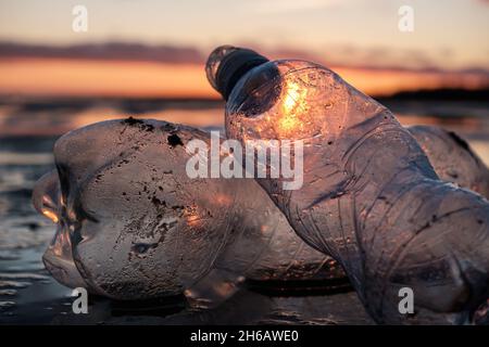 Primo piano di bottiglie di plastica gettate sulla riva nella retroilluminazione. Inquinamento ambientale causato dalla plastica. Confezione riciclabile. Foto Stock