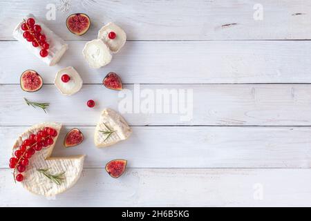 camembert e formaggio di capra decorati con fette di fichi, ribes rosso e rosmarino, su sfondo bianco di legno, vista dall'alto, spazio copia Foto Stock