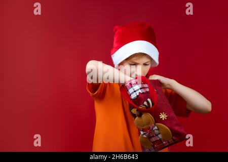 Un ragazzo in un cappello di Santa rummages in una borsa di Natale in cerca di regali Foto Stock