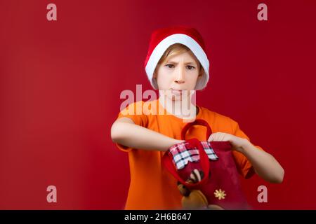 Un ragazzo in un cappello di Santa rummages in una borsa di Natale in cerca di regali Foto Stock