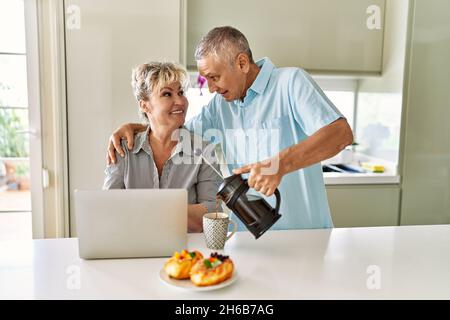 Coppia caucasica senior che ha fatto colazione utilizzando un computer portatile in cucina. Foto Stock