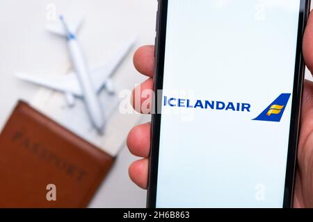 Applicazione Icelandair Airline sullo schermo dello smartphone mans hand. Un aeroplano giocattolo bianco e un passaporto si trovano su un tavolo con una superficie leggera.Novembre 2021, San Francisco, USA Foto Stock