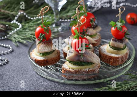 Canape con aringhe salate, cetrioli, patate bollite e pomodori ciliegini su crostini di segale su sfondo grigio. Foto Stock