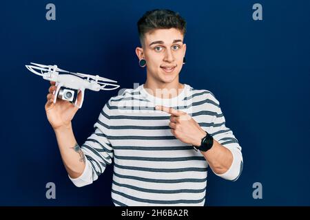 Giovane ragazzo caucasico con le orecchie dilatazione tenendo il drone sorridendo felice puntando con mano e dito Foto Stock