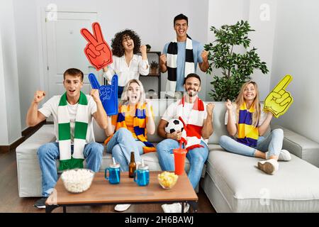 Gruppo di amici che sostengono la squadra di calcio che guarda la tv a casa seduta sul divano urlando orgoglioso, celebrando la vittoria e il successo molto eccitato con r Foto Stock