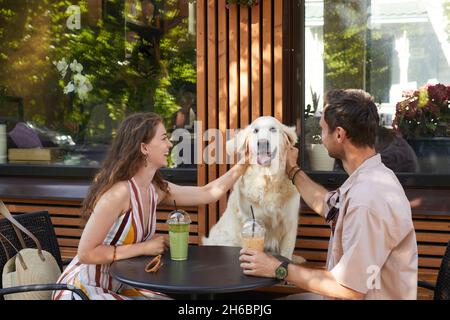 Ritratto di coppia felice con cane seduto a tavola insieme in un bar all'aperto e ridendo, spazio copia Foto Stock