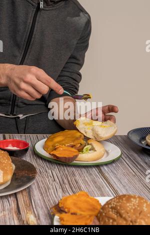 Le mani spalancano senape gialla sulla parte superiore di un boccale di cheeseburger e lattuga Foto Stock