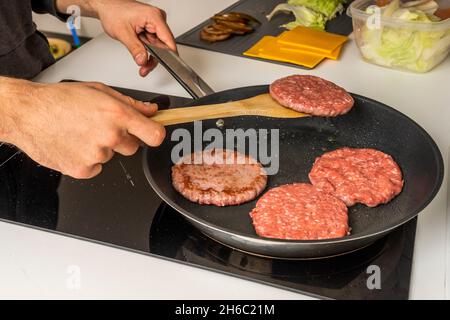 Cucinare diversi hamburger di manzo su una griglia elettrica per mano di un giovane uomo Foto Stock