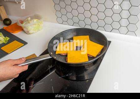 Fette di formaggio cheddar su filetti di hamburger di manzo cucinati sulla griglia elettrica Foto Stock