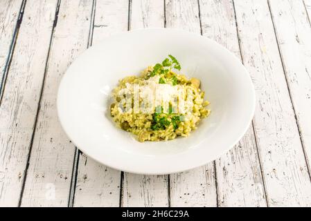 risotto con asparagi, funghi e prezzemolo condito con formaggio grattugiato su un piatto bianco intenso Foto Stock