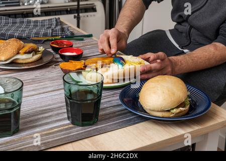 Le mani del giovane spalmano senape sulla parte superiore del pane di un hamburger Foto Stock