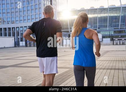 Vista posteriore di una coppia sportiva di mezza età che rimane attiva, che corre insieme in ambiente urbano Foto Stock