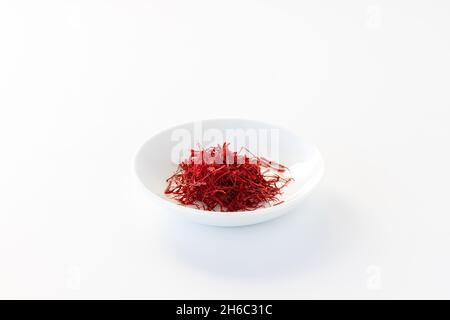 Primo piano di un piccolo piatto pieno di fili di zafferano su sfondo bianco. Foto Stock