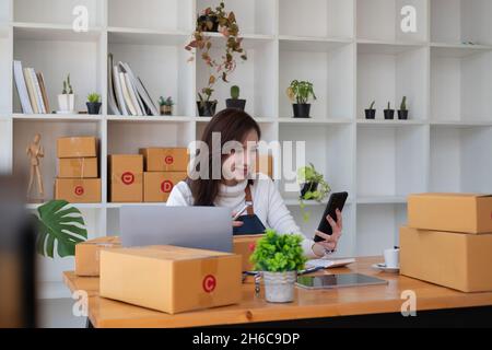 Avvio piccole imprese imprenditore SME freelance, ritratto giovane donna che lavora a casa ufficio, BOX, smartphone, laptop, online, marketing, packaging Foto Stock