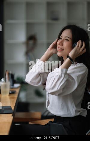 Ritratto bella ragazza asiatica ascoltare la musica con cuffie e leggere libri mentre si siede al tavolo nella caffetteria Foto Stock