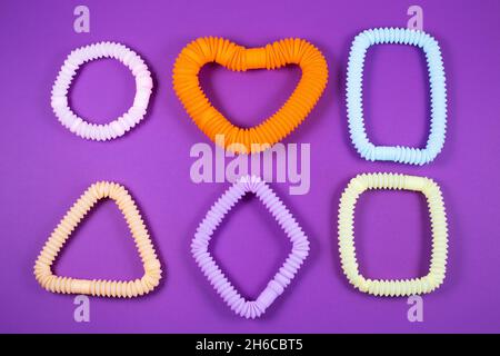 Tubi pop colorati sotto forma di figure geometriche su sfondo viola. Giocattoli antistress per le dita per adulti e bambini. Foto Stock