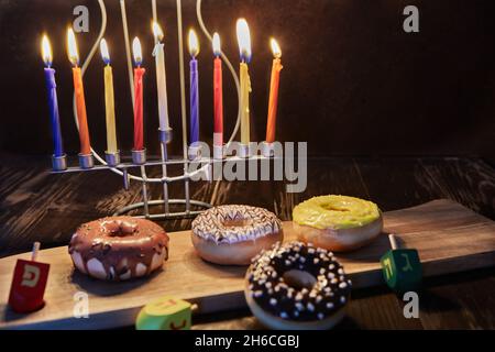 Happy Hanukkah e Hanukkah Sameach - candeliere ebraiche tradizionali con candele, ciambelle e cime giranti su sfondo di legno marrone. Foto Stock