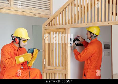 Costruttori che lavorano in casa in costruzione, stanno installando scala e prese di legno Foto Stock