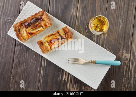 Torta di mele con fette di vaniglia affettate con un bicchiere di liquore, su sfondo di legno. Cucina gourmet francese Foto Stock