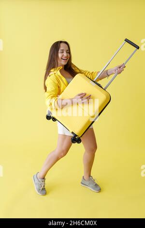 Donna gioiosa con carrello bagaglio in piedi in studio Foto Stock
