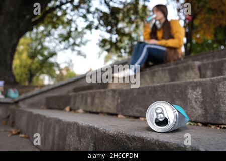 Una lattina di alluminio spremuta e un adolescente che beve energia seduto sulle scale. Foto Stock