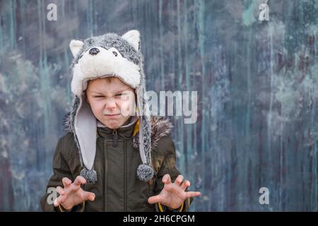 Il ruggito di un lupo. Bambino in un cappello lupo su sfondo grigio, all'aperto. Foto di alta qualità Foto Stock