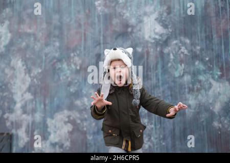 Il ruggito di un lupo. Bambino in un cappello lupo su sfondo grigio, all'aperto. Foto di alta qualità Foto Stock