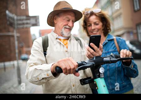 Primo piano di felice coppia di turisti anziani codice di scansione per noleggiare uno scooter insieme all'aperto in città Foto Stock