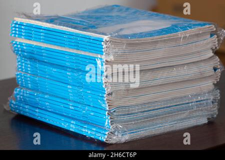 Stack di notebook. Una confezione di taccuini blu in cellophane sul tavolo in una classe. Pila di libri di esercizi. Carta rigata. Imballaggio a scacchi Foto Stock