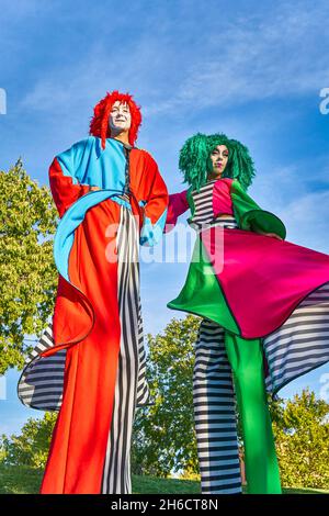Dal basso di divertenti spettacoli di artisti su palafitte in colorati costumi clown e parrucche si levano insieme nel parco verde e durante gli eventi festosi Foto Stock