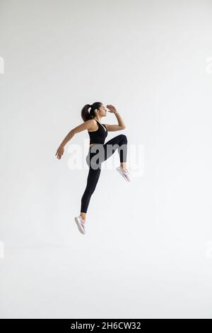 Giovane donna elegante è impegnata in aerobica saltando esercizi isolati su sfondo bianco. Allenatore sportivo fit pulcino. Foto Stock